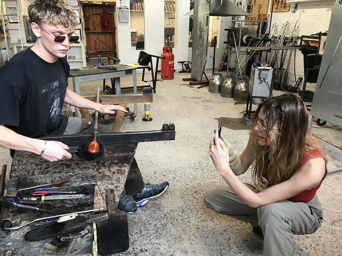 Peter Dupont working with hot glass while Breanna Box photographs him
